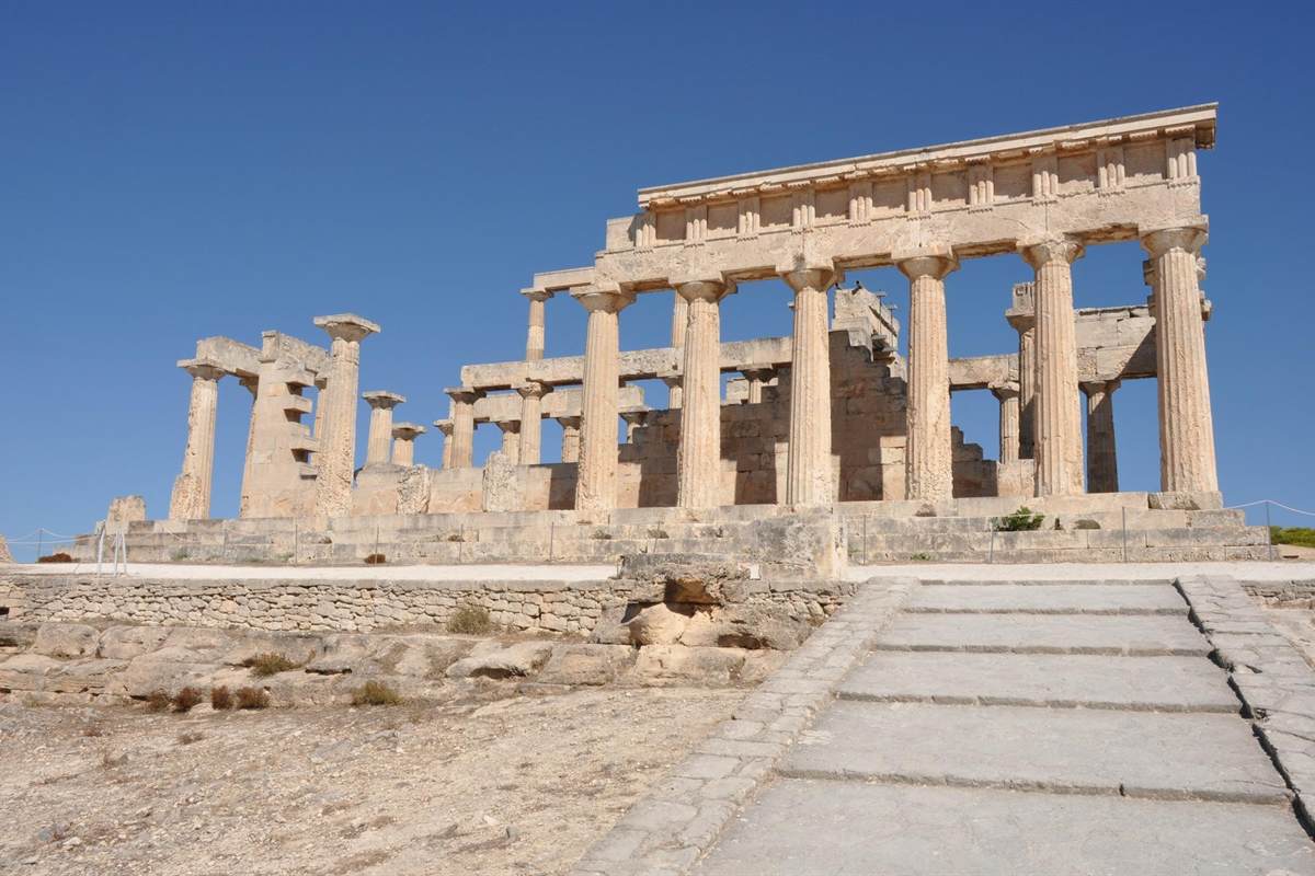 Hydra Poros and Aegina day cruise from Athens: the pale limestone Doric columns and beams of the Temple of Aphaia on Aegina against a deep blue sky, with a wide stone path of steps in the foreground